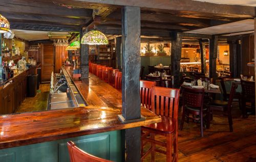 Cozy restaurant interior featuring a wooden bar, high chairs, and warm lighting with a rustic ambiance.