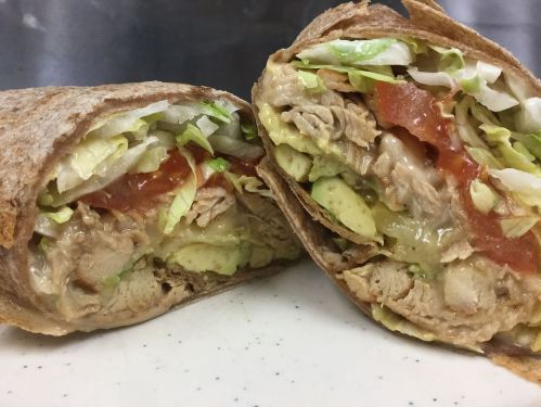 A close-up of a sliced wrap filled with chicken, lettuce, tomato, and avocado, showcasing its fresh ingredients.