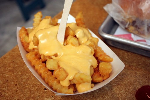 A serving of crinkle-cut fries topped with melted cheese sauce in a paper tray.