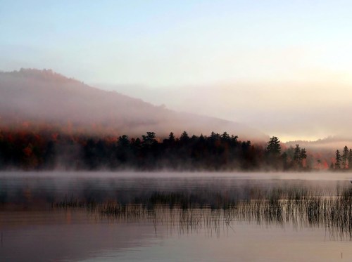 A serene lake at dawn, surrounded by misty mountains and autumn foliage, reflecting calm waters.