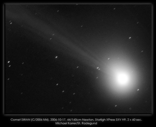 Black and white image of Comet SWAN with a bright nucleus and a long tail, surrounded by stars.