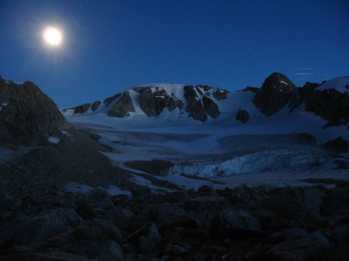 A serene night scene of a snowy mountain landscape illuminated by a bright full moon.