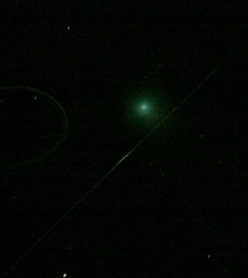 A bright green comet with a faint tail, surrounded by dark space and distant stars.