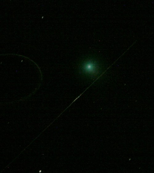 A bright green comet with a faint tail, surrounded by dark space and distant stars.