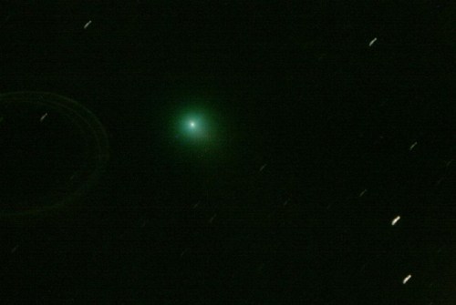 A bright green comet surrounded by stars, set against a dark night sky with streaks indicating star movement.