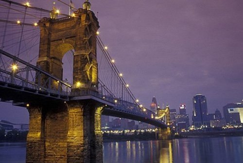 Cincinnati's illuminated suspension bridge at dusk, with city skyline reflected in the water.