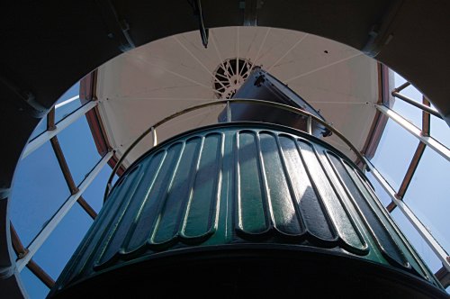 View looking up from inside a lighthouse, showcasing the circular structure and glass windows above.