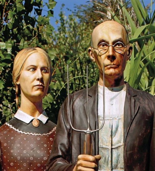 Two life-sized sculptures of a farmer and a woman, standing together in a garden, with greenery in the background.