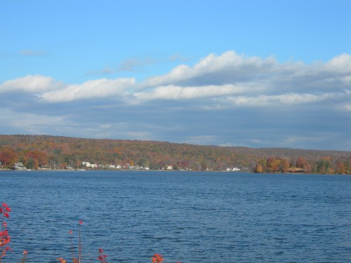 A serene lake surrounded by colorful autumn foliage under a blue sky with fluffy clouds.