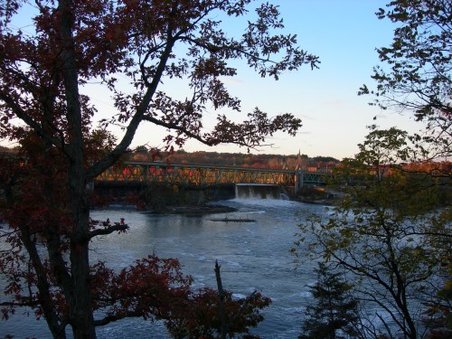 A scenic view of a bridge over a river, framed by autumn trees and a clear blue sky.