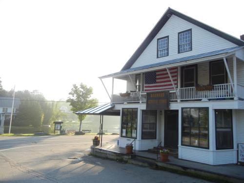 A quaint white building with an American flag, featuring a porch and flower pots, in a foggy rural setting.