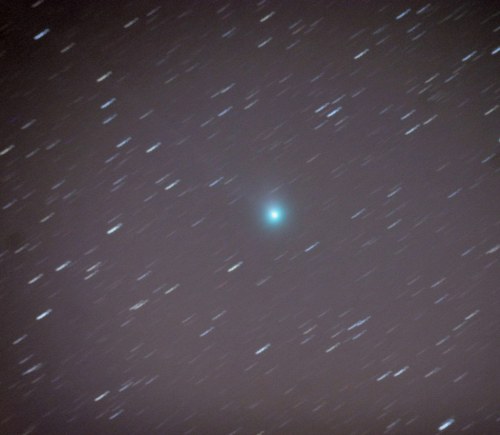 A blurred image of a bright blue comet surrounded by scattered stars against a dark sky.