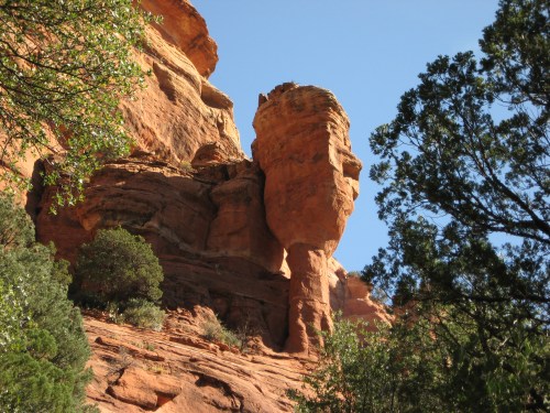 A towering rock formation surrounded by greenery under a clear blue sky.