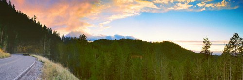 A winding road through a forested landscape at sunset, with vibrant clouds and a colorful sky.