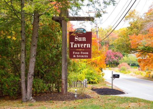 A sign for Sun Tavern, featuring "Fine Food & Spirits," surrounded by colorful autumn foliage and a rural road.