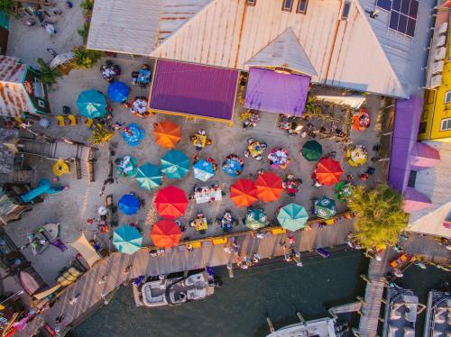 Aerial view of a vibrant outdoor dining area with colorful umbrellas and people enjoying meals by the water.