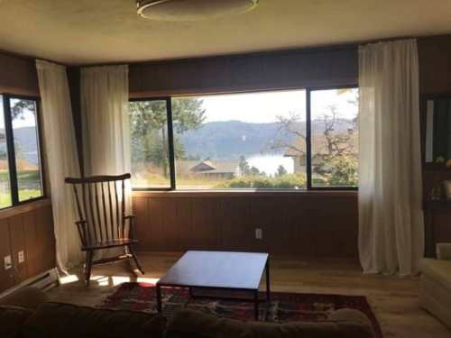 Cozy living room with a rocking chair and a view of a lake and mountains through large windows.