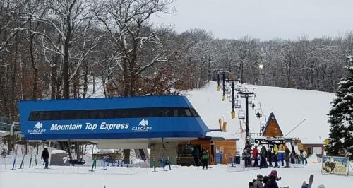 Ski resort scene with a blue lift station, snow-covered slopes, and skiers waiting in line at the base.