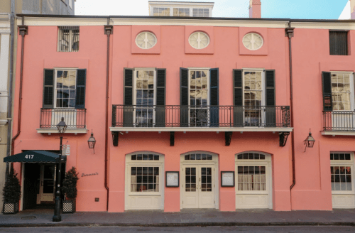 A pink building with black shutters and balconies, featuring large windows and a welcoming entrance.