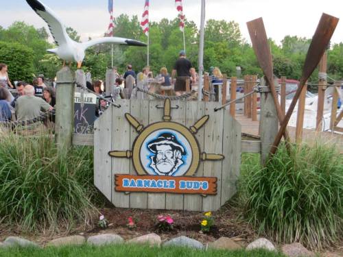 Sign for Barnacle Bud's with a nautical theme, surrounded by greenery and people enjoying the outdoor space.