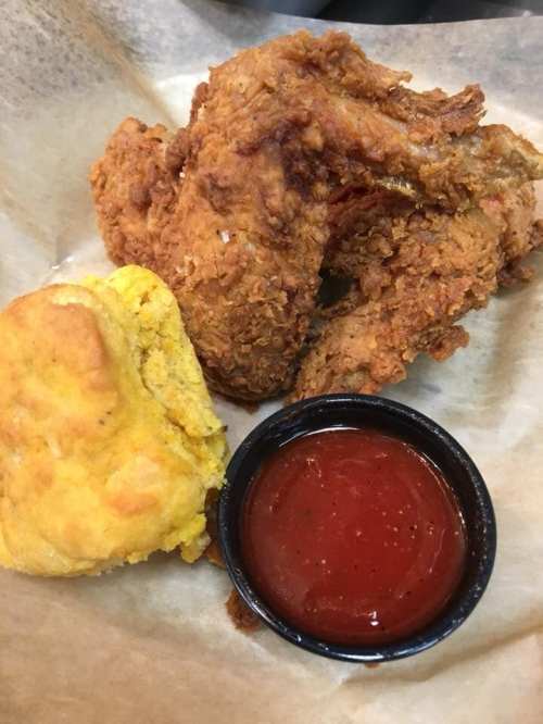 Crispy fried chicken wings with a side of cornbread and a small cup of dipping sauce on parchment paper.