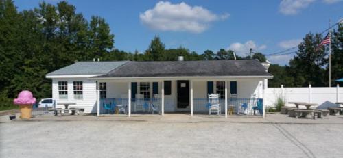 A small white building with blue accents, outdoor seating, and a large ice cream cone statue in front.