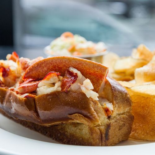 A delicious lobster roll on a toasted bun, served with coleslaw and crispy potato chips.