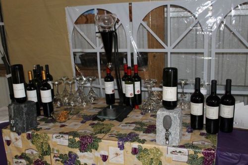 A wine display featuring various bottles, glasses, and snacks on a table with a grape-themed tablecloth.
