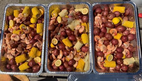 Three trays filled with shrimp, corn, potatoes, and lemon slices, arranged for a seafood feast.