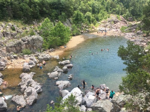 A scenic river with people swimming and relaxing among rocky shores and lush greenery.
