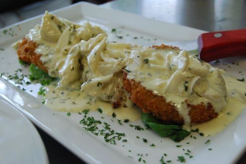A plate of breaded chicken topped with creamy sauce and herbs, served on a bed of greens.