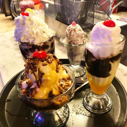 A tray of four delicious ice cream sundaes topped with whipped cream and cherries, featuring various flavors and toppings.