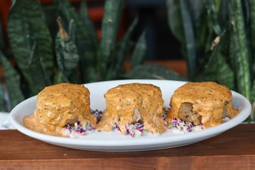 Three meatloaf portions topped with creamy sauce, served on a bed of shredded cabbage, with green plants in the background.
