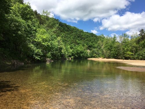 A serene river flows through a lush green landscape under a partly cloudy sky.