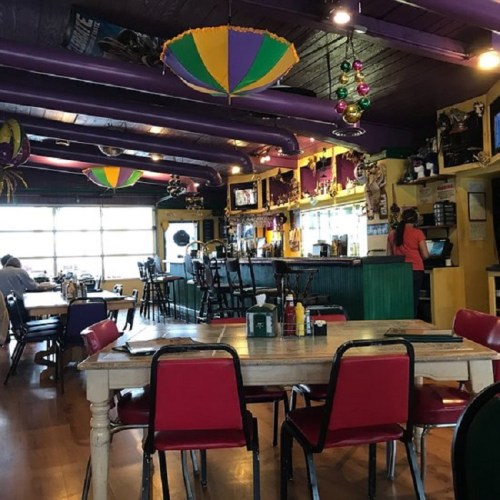 Colorful restaurant interior with purple beams, festive decorations, a bar area, and red chairs at wooden tables.