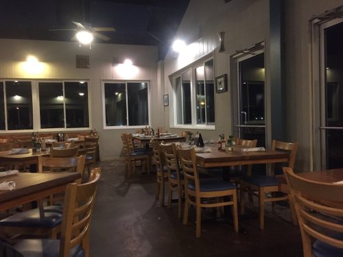 Interior of a restaurant with empty tables, wooden chairs, and large windows, illuminated by soft lighting.