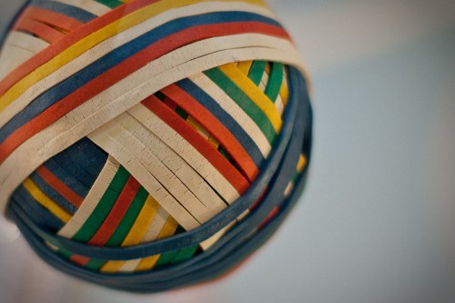 A close-up of a colorful rubber band ball made of various striped bands in red, blue, green, and yellow.