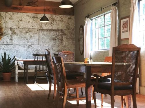 A cozy dining area with wooden tables and chairs, large windows, and natural light illuminating the space.