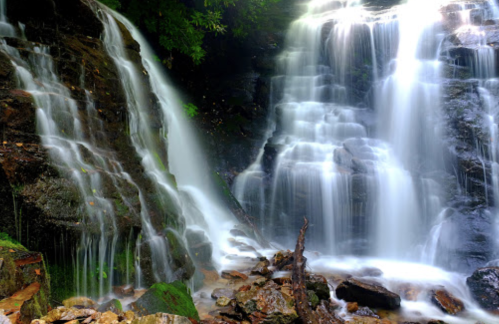 A serene waterfall cascading over rocks, surrounded by lush greenery and smooth stones at the base.
