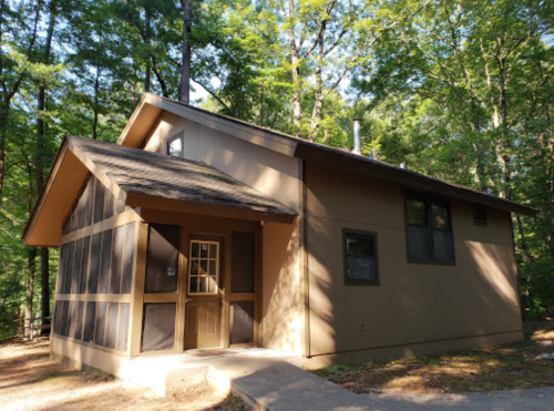 A modern cabin surrounded by trees, featuring a screened porch and a welcoming front door.
