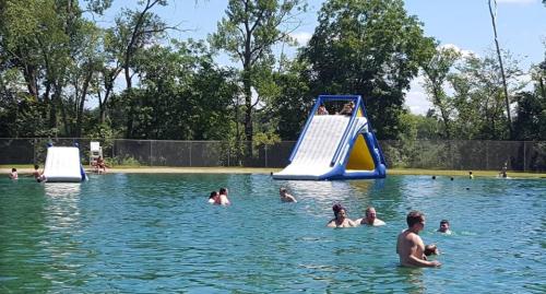 A sunny outdoor pool scene with people swimming and a large inflatable slide in the background.