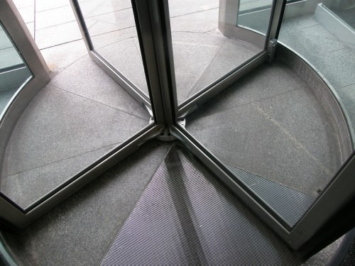 A close-up of a glass revolving door with a textured floor and metal grating at the entrance.