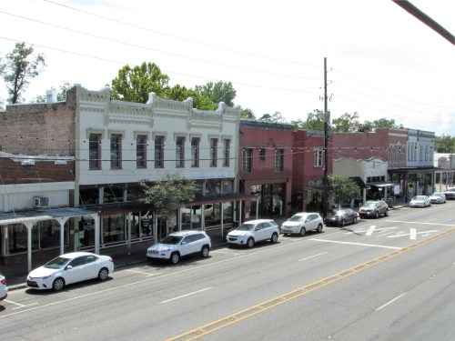 A view of a small town street lined with historic buildings and parked cars under a partly cloudy sky.