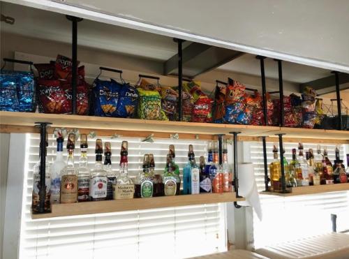 A shelf displaying various snacks in bags and a collection of liquor bottles underneath.