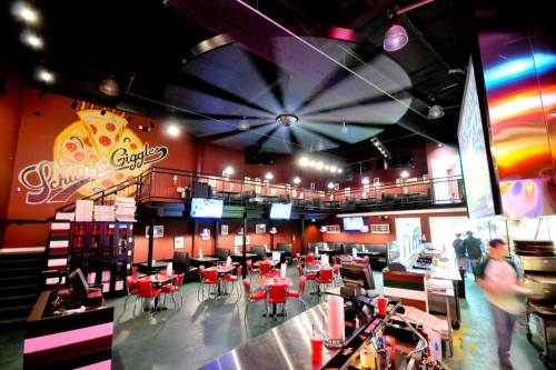 Interior of a vibrant restaurant with red chairs, large screens, and a mural of pizza on the wall.
