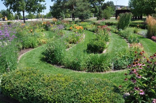 A lush garden with winding paths, vibrant flowers, and greenery under a clear blue sky.