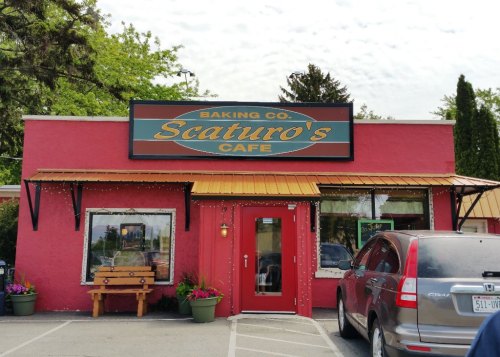 A pink cafe building with a sign reading "Scaturro's Cafe" and a wooden bench outside, surrounded by flowers.
