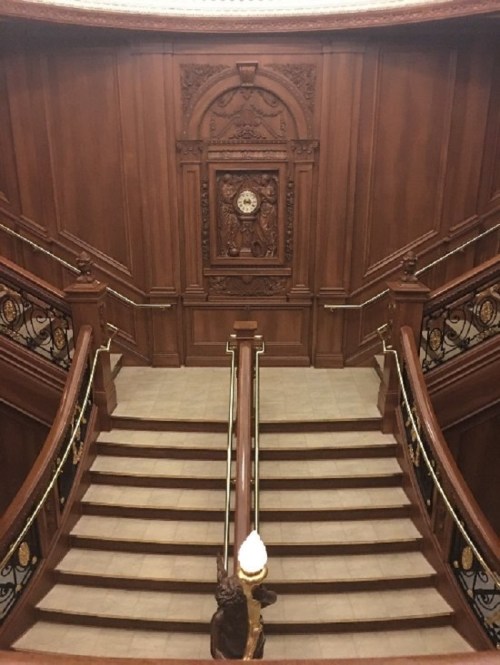 Elegant wooden staircase with ornate railings and a decorative wall clock, leading down to a tiled floor.