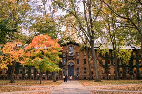 A historic building surrounded by vibrant autumn trees, with two people walking along a path in the foreground.