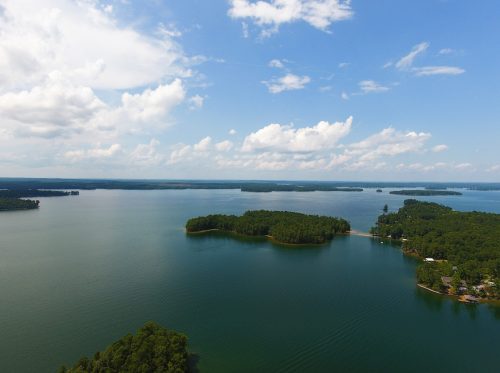 Aerial view of a serene lake with lush green islands and a blue sky dotted with clouds.